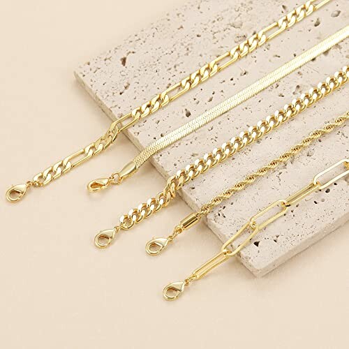 Various gold chain bracelets on a textured surface